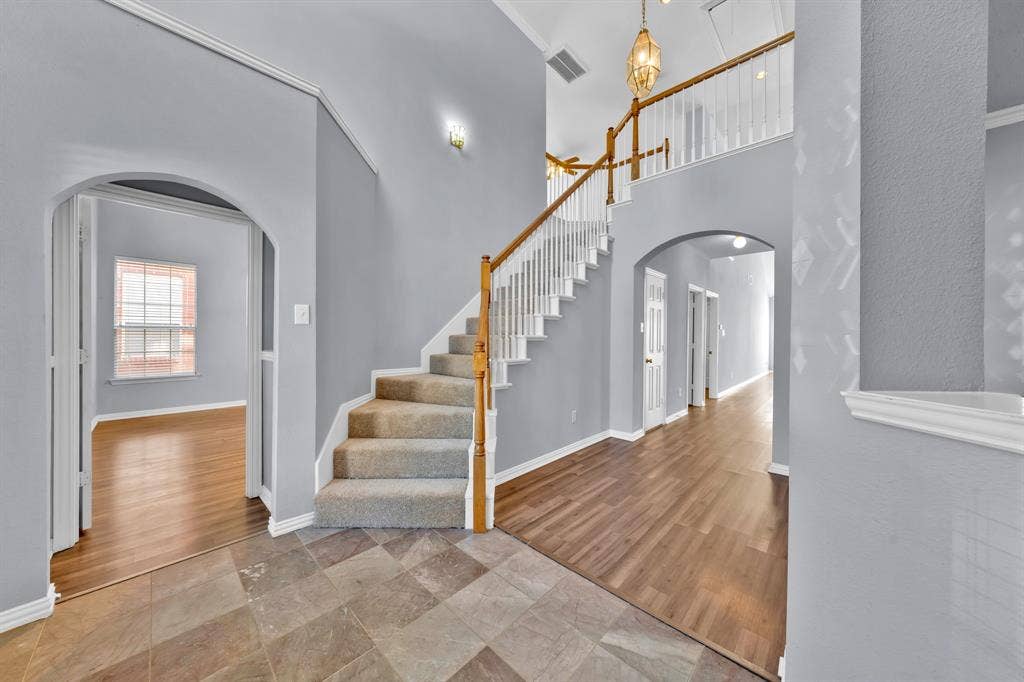 Two-story foyer with high ceilings, an arched entry, wood-finish flooring, and a carpeted staircase with wood handrails
