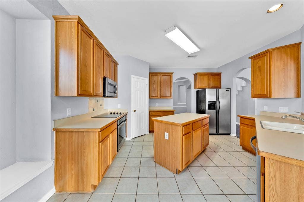 Kitchen featuring a central island, wood-finish cabinetry, tile flooring, and integrated stainless steel appliances