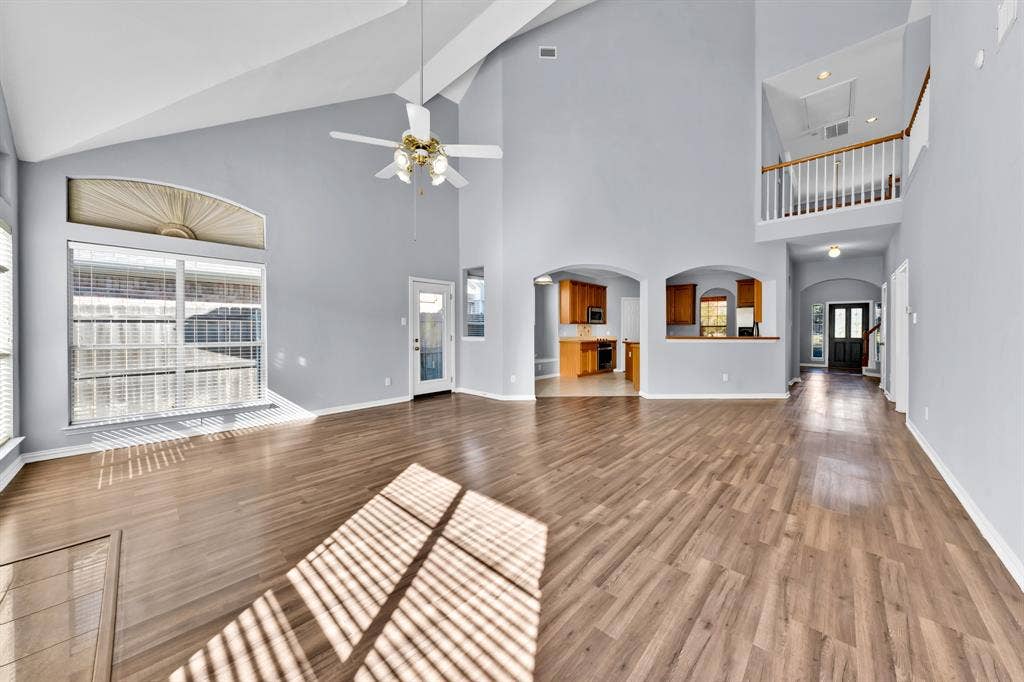 Vaulted ceiling with a ceiling fan, wood-finish flooring, arched doorways, interior balcony, and a paneled front door