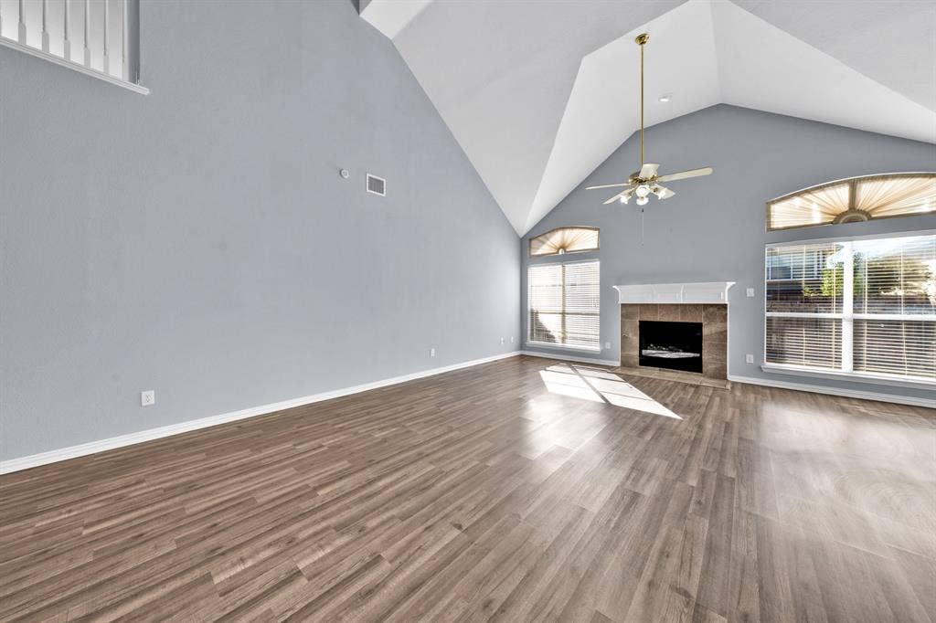 Spacious living area featuring wood-finish flooring, vaulted ceilings, a fireplace with a tile surround, a classic mantel, and multiple arched windows