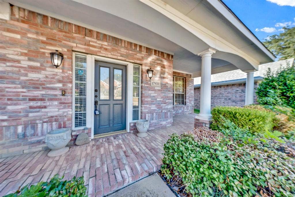 Brick facade with a covered entry featuring white columns, a dark panel door with glass inserts, and flanking wall sconces