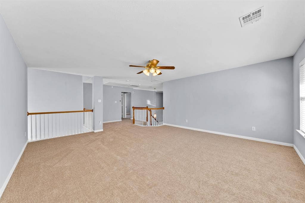 Spacious carpeted room featuring a ceiling fan, light blue walls, white trim, and white railings with wood-finish tops