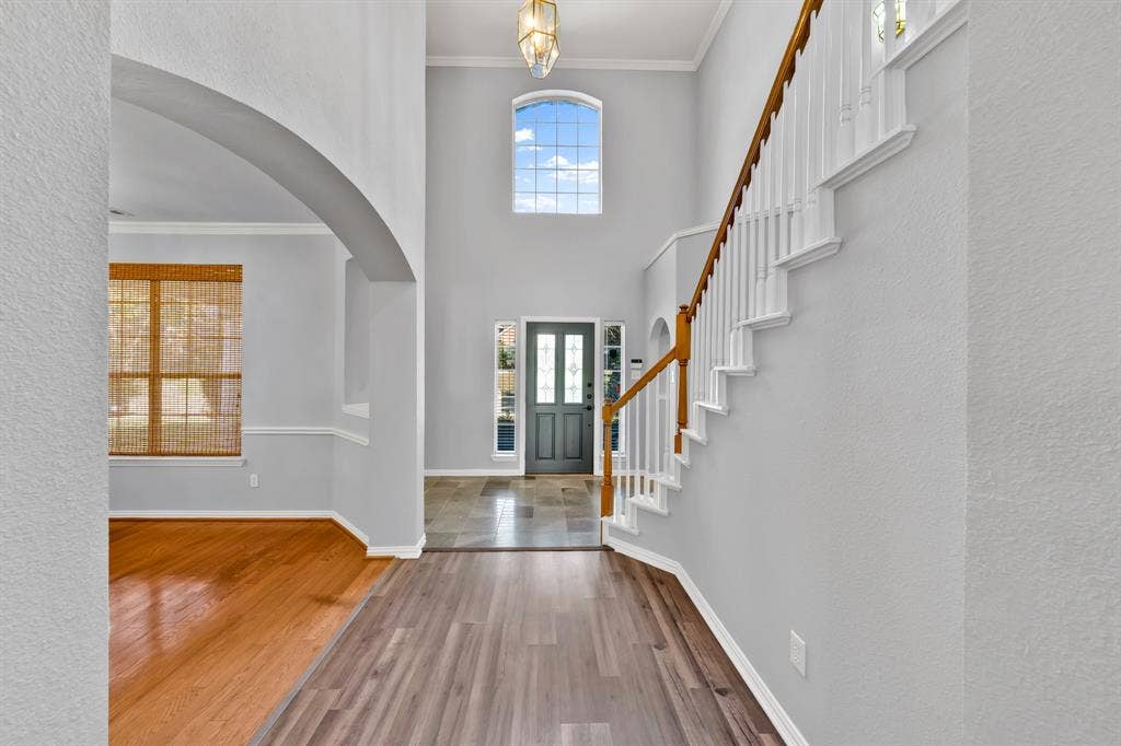 Two-story foyer with a grand staircase featuring a wood handrail, an arched doorway, and a prominent arched window