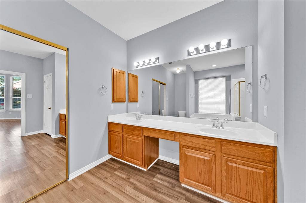 Vanity with dual sinks, overhead lighting, wood-finish flooring, and built-in cabinetry