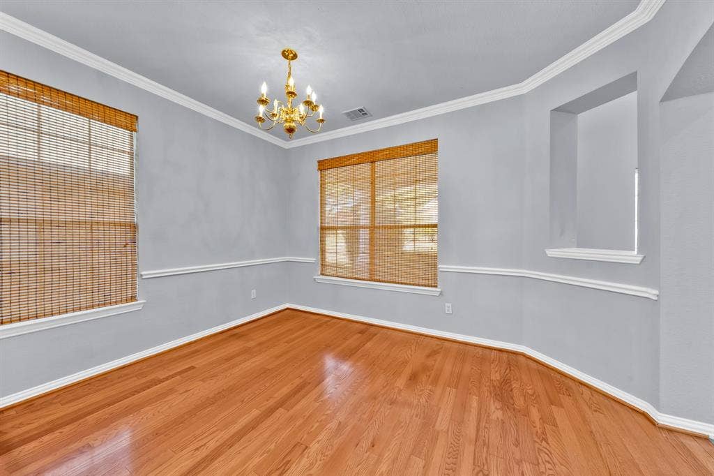 Wood-finish flooring, crown molding, chair rail molding, recessed wall feature, and a brass chandelier
