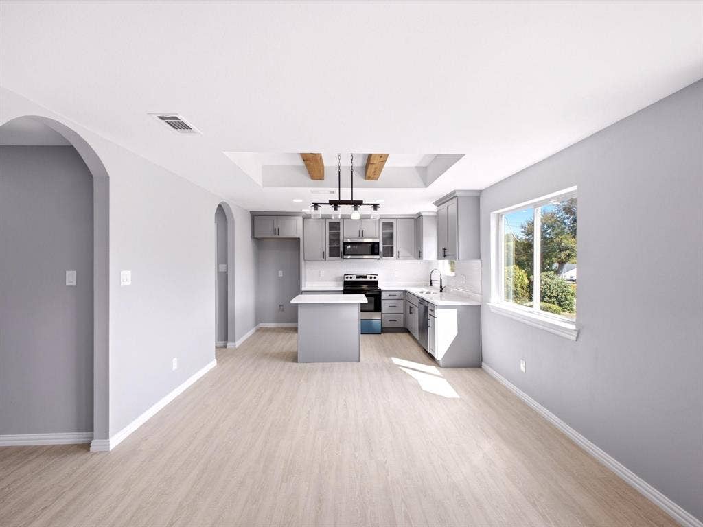 1727 Mentor Avenue, Dallas, TX 75216 Light wood-finish flooring, arched doorways, kitchen island with seating, recessed ceiling feature with wood beams, and a modern kitchen with gray cabinetry