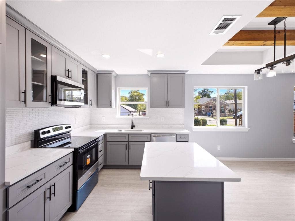 1727 Mentor Avenue, Dallas, TX 75216 Kitchen featuring gray shaker-style cabinetry, white quartz countertops, a white subway tile backsplash, stainless steel appliances, and a central island with a waterfall edge