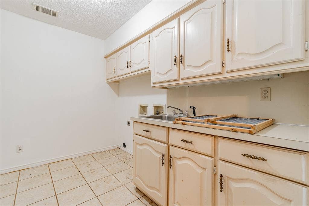 4320 Hickox Road, Rowlett, TX 75089 Functional laundry area featuring upper and lower cabinetry, a utility sink, and tile flooring