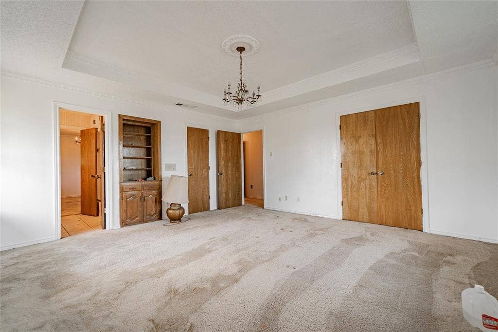 4320 Hickox Road, Rowlett, TX 75089 Tray ceiling with decorative molding, chandelier lighting, built-in shelving, and wood doors