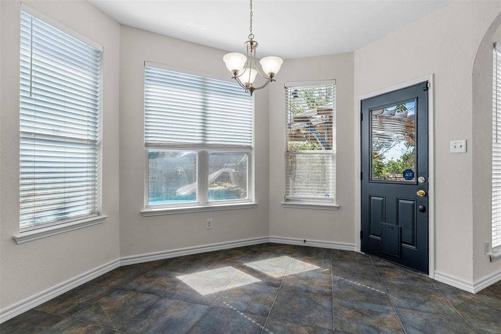 Bay window with multiple windows, overhead chandelier, and a paneled door with glass insert, all above dark-toned tile flooring