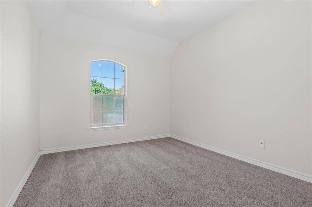 Arched window with exterior views, vaulted ceiling, neutral wall color, and grey carpet flooring