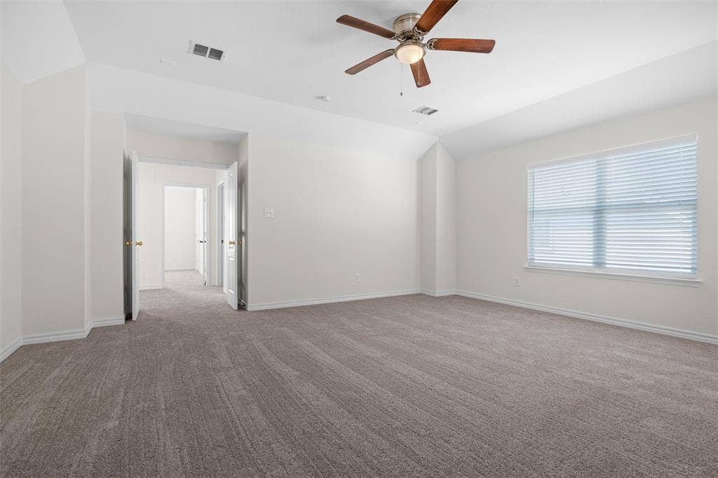 Spacious room with plush carpeting, a large window, a ceiling fan with integrated lighting, and multiple interior doorways