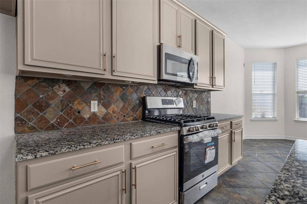 Kitchen featuring granite-style countertops, under-cabinet lighting, stainless steel appliances, a gas range, and a tiled backsplash