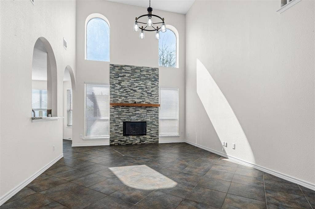 Vaulted ceiling with a contemporary chandelier, arched windows, tile flooring, and a fireplace with a stone surround and wood mantle
