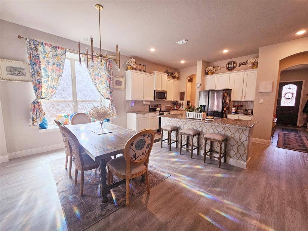 Open-concept kitchen and dining area featuring wood-finish flooring, white cabinetry, recessed lighting, and a kitchen island with seating