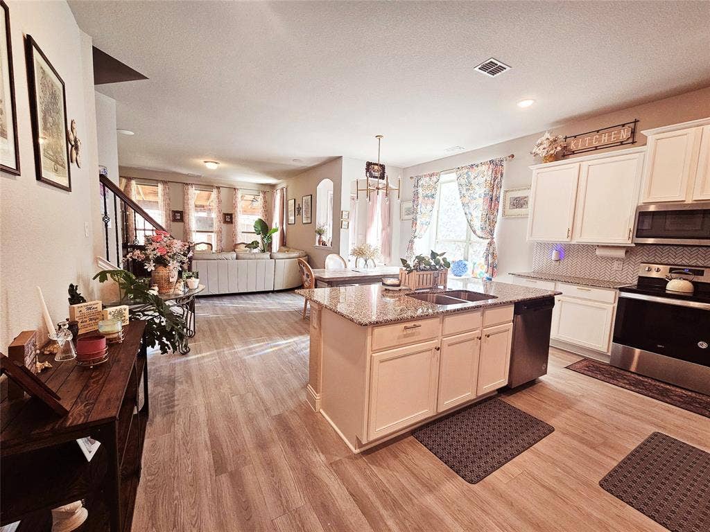 Wood-finish flooring throughout, kitchen island with granite countertop and double-basin sink, white cabinetry with integrated appliances, and a tile backsplash