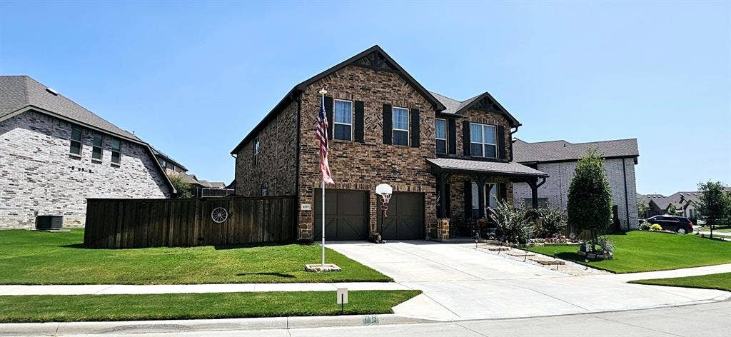 Brick exterior with a dark roof, two-car garage, covered entry, and a manicured lawn