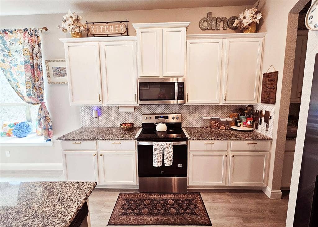 White cabinetry, granite countertops, herringbone tile backsplash, stainless steel appliances, and wood-finish flooring