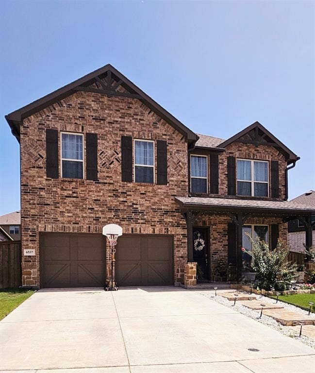 Brick exterior facade with decorative gables, covered front porch, and an attached two-car garage