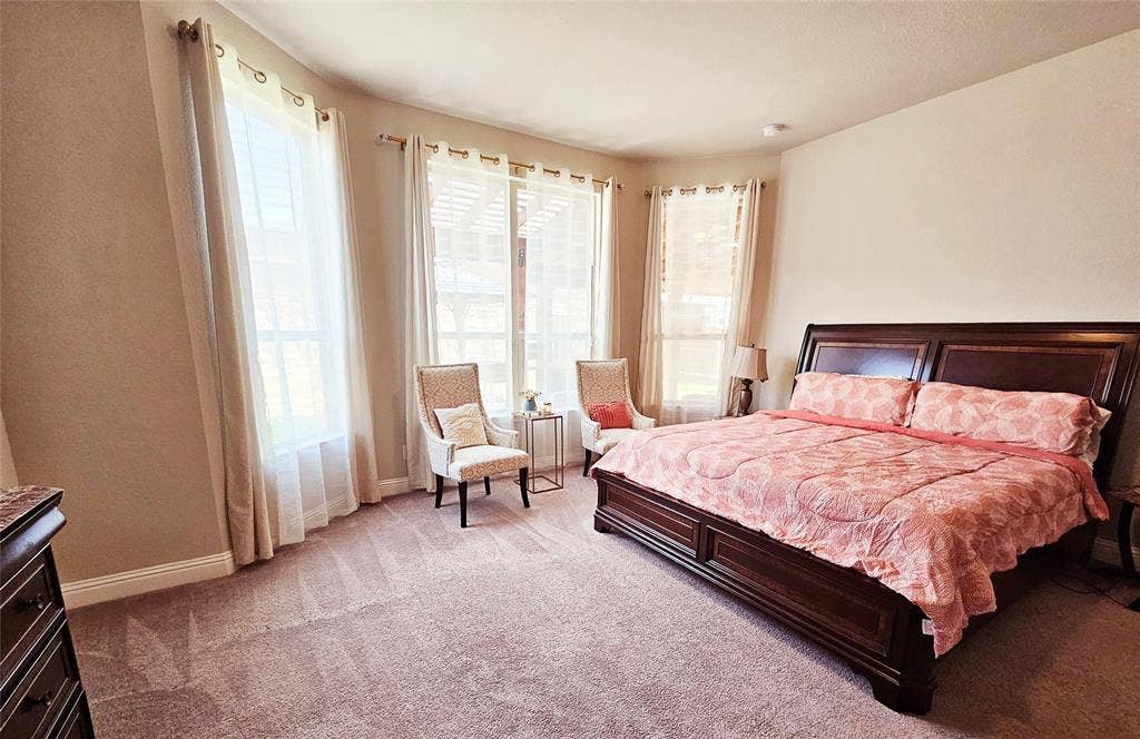 Carpeted flooring with a prominent bay window area, featuring multiple windows with drapery rods and sheer privacy coverings