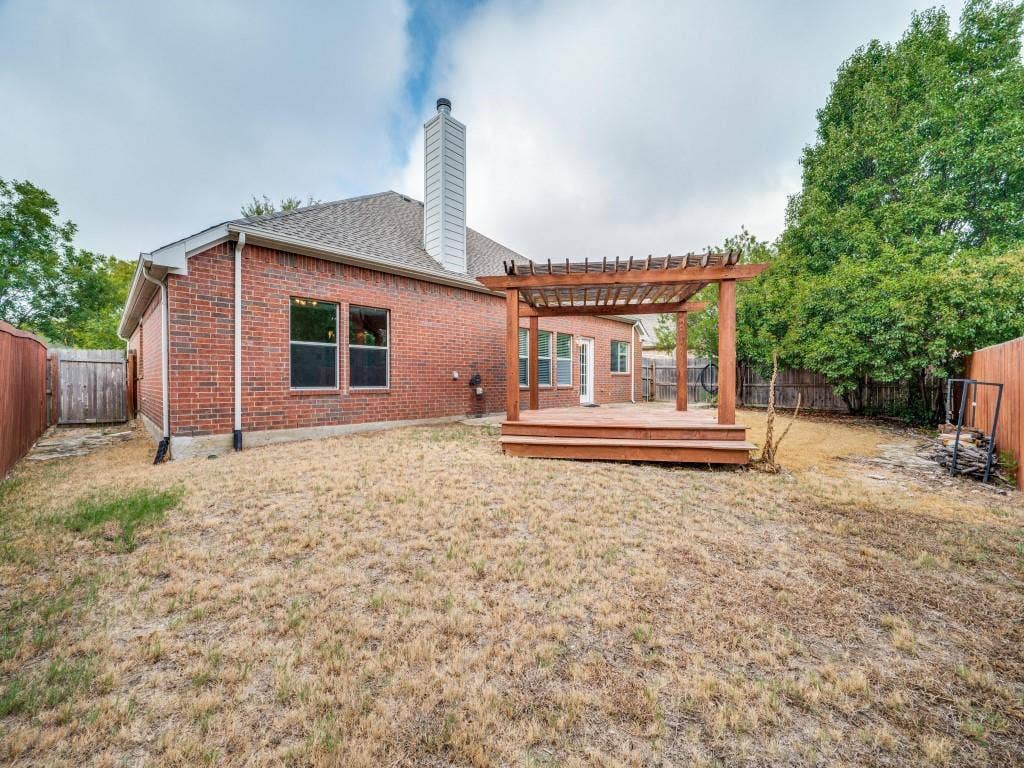 5604 Parkplace Drive, Denton, TX 76226 Brick exterior with a prominent chimney, wood-tone decking, and a coordinating pergola