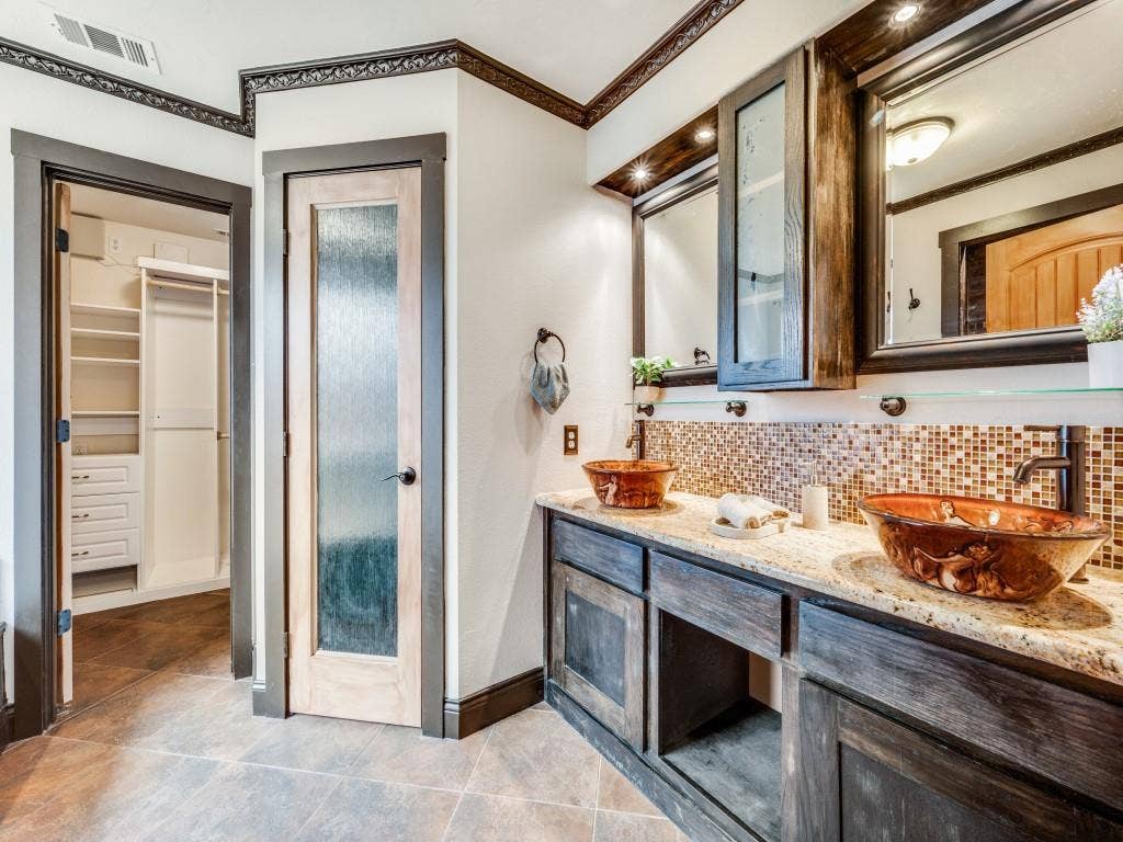 5604 Parkplace Drive, Denton, TX 76226 Dual vessel sinks, tile flooring, mosaic tile backsplash, custom wood cabinetry, and a walk-in closet with built-in shelving