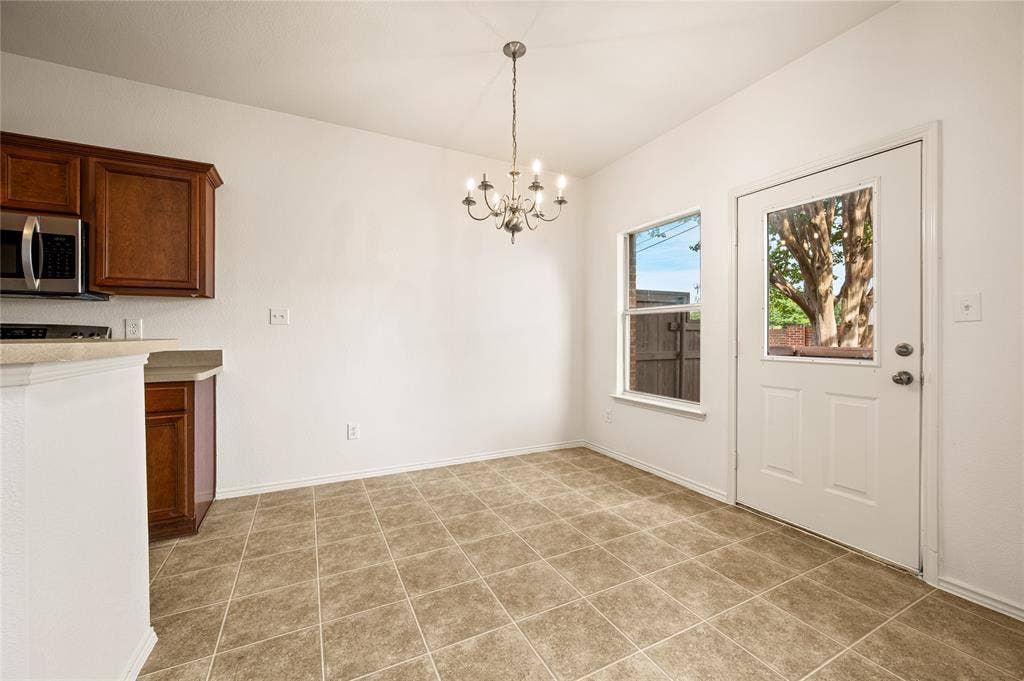 4535 Woodsboro Lane, Plano, TX 75024 Vaulted ceiling with chandelier lighting, tile flooring, wood-finish cabinetry, stainless steel microwave, and exterior door with integrated window