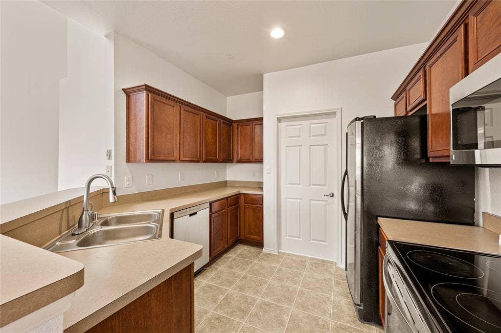 4535 Woodsboro Lane, Plano, TX 75024 Kitchen featuring wood-finish cabinetry, solid surface countertops, a stainless steel double-basin sink with a gooseneck faucet, a built-in dishwasher, and tile flooring