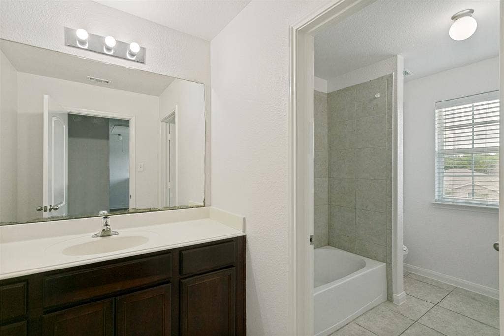 Bathroom featuring a dark wood-finish vanity with an integrated sink, a large wall-mounted mirror, and a three-bulb vanity light fixture
