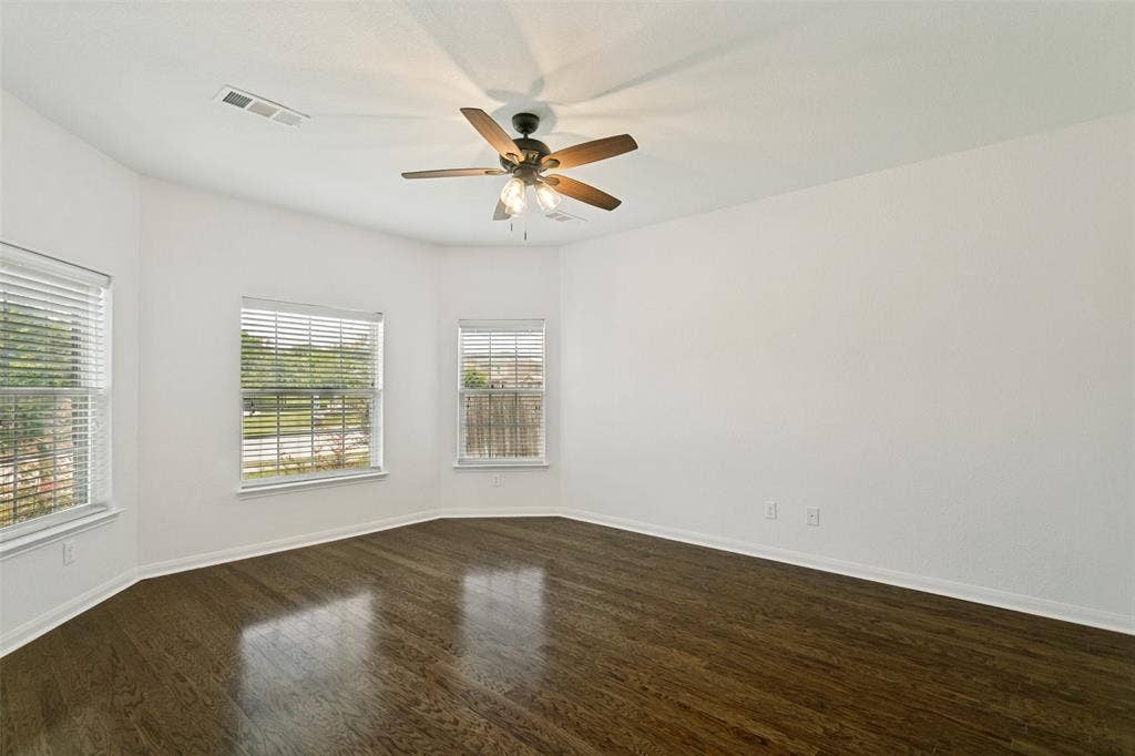 Interior space featuring dark wood-finish flooring, white walls, multiple windows with blinds, and a ceiling fan with integrated lighting