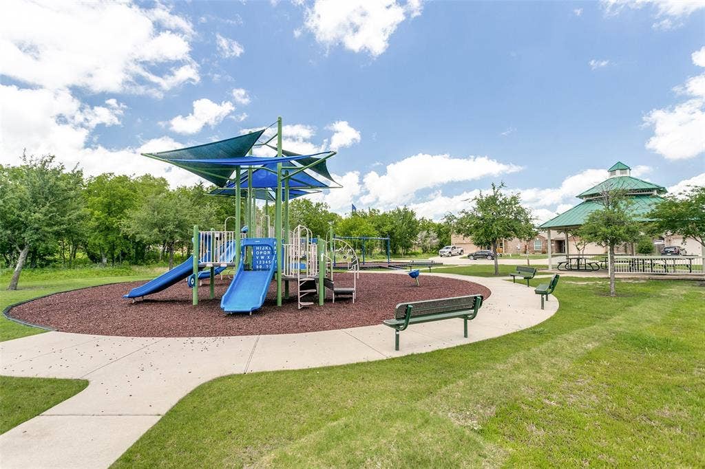 Community playground featuring a multi-level play structure with slides and swings, shaded by blue canopies