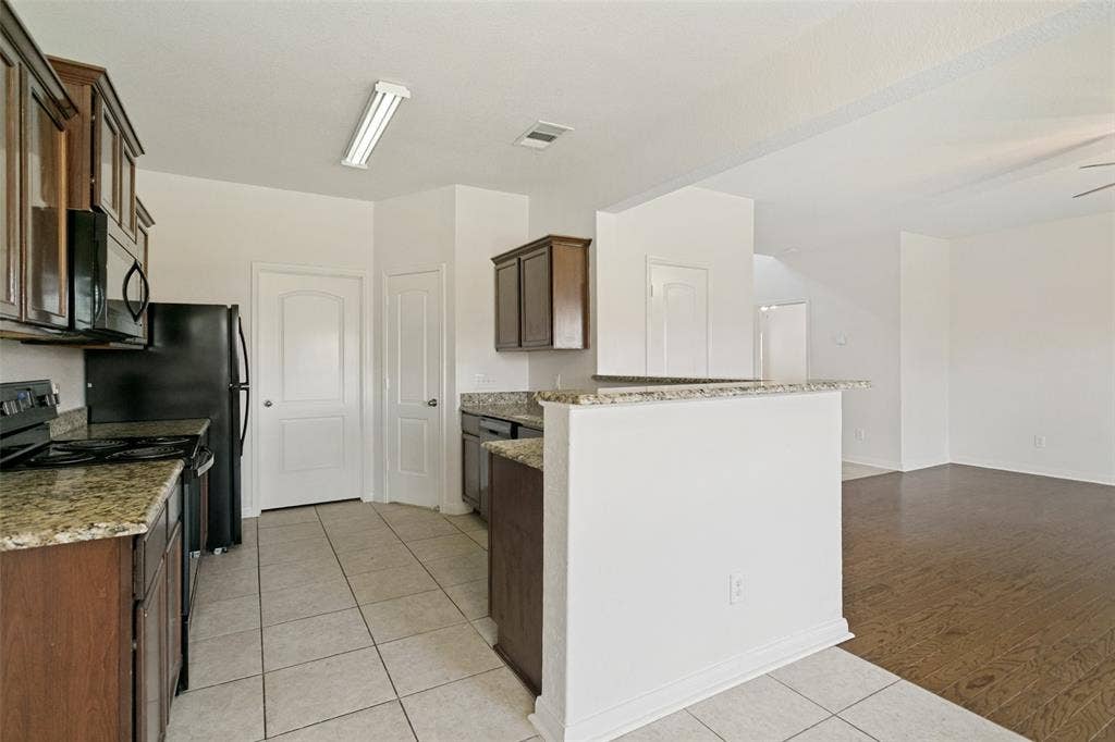 Kitchen featuring wood-finish cabinetry, stone countertops, black appliances, and tile flooring
