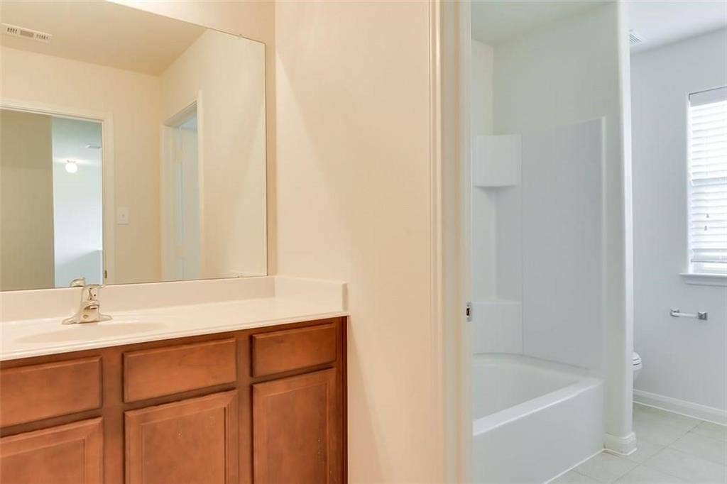 Bathroom featuring a wood-finish vanity with a white countertop, an integrated sink, and a large wall-mounted mirror