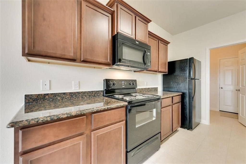 Kitchen featuring wood-finish cabinetry, speckled countertops, and a full suite of black appliances
