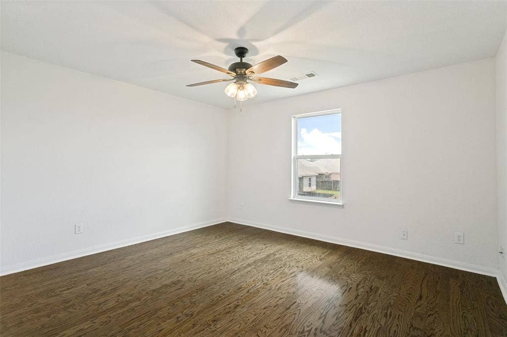 Spacious room featuring wood-finish flooring, white baseboards, and a ceiling fan with integrated lighting