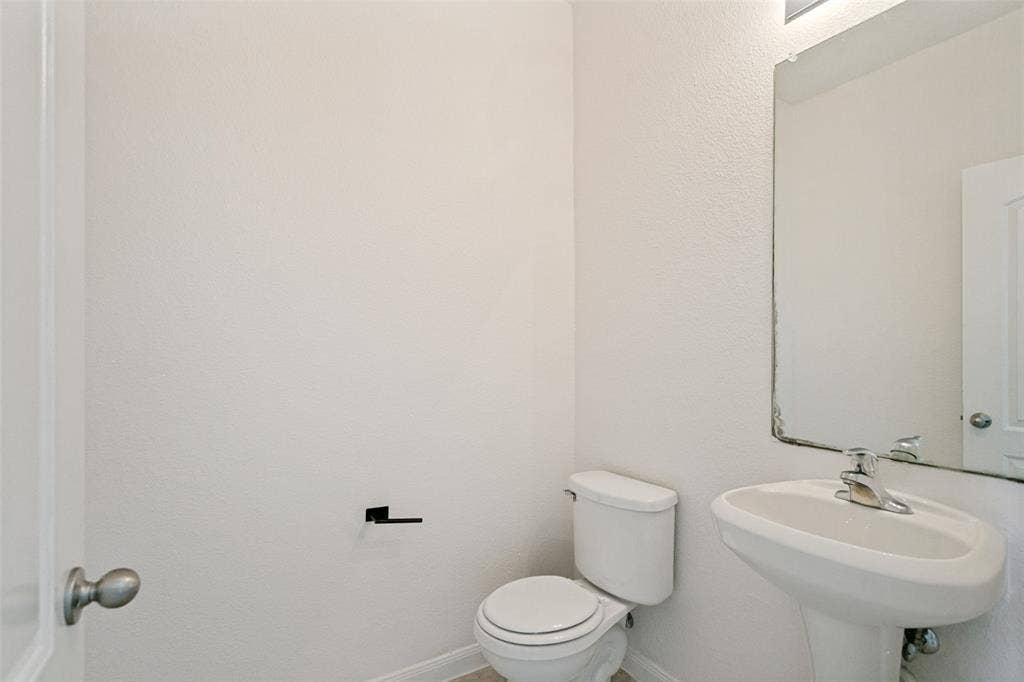 Powder room featuring a pedestal sink with chrome faucet, a white toilet, and a wall-mounted mirror