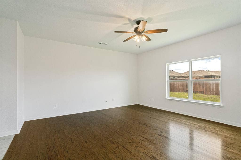 Spacious room featuring wood-finish flooring, a contemporary ceiling fan with integrated lighting, and a large window offering exterior views