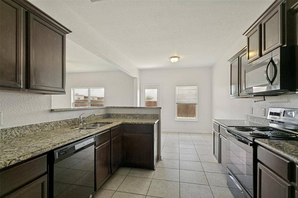 Kitchen featuring dark wood-finish cabinetry, speckled countertops, dual basin sink, and stainless steel appliances including a dishwasher, electric range, and built-in microwave