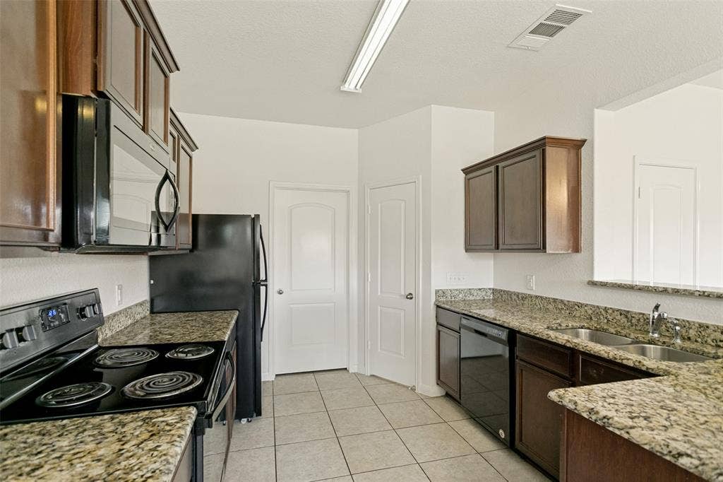 Kitchen featuring black appliances, granite countertops, wood-finish cabinetry, tile flooring, and a double-basin sink