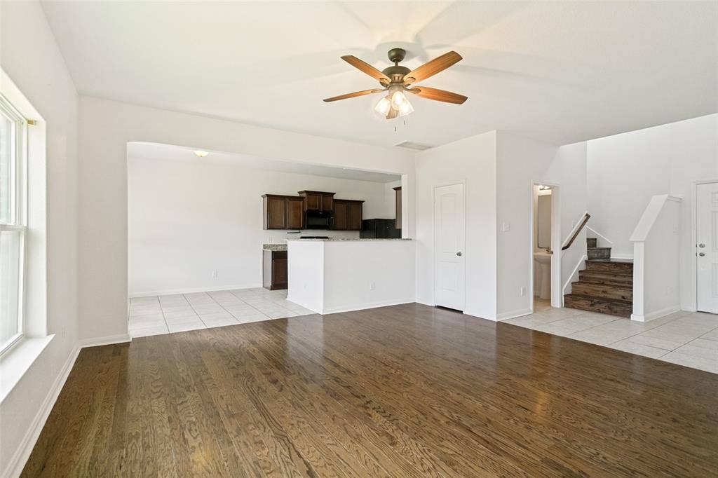 Spacious living area featuring wood-finish flooring, a ceiling fan with integrated lighting, and an open concept layout to the kitchen
