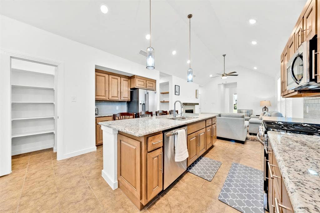 3928 Bison Lane, Crandall, TX 75114 Kitchen featuring a large central island with a sink, granite countertops, stainless steel appliances, and wood cabinetry