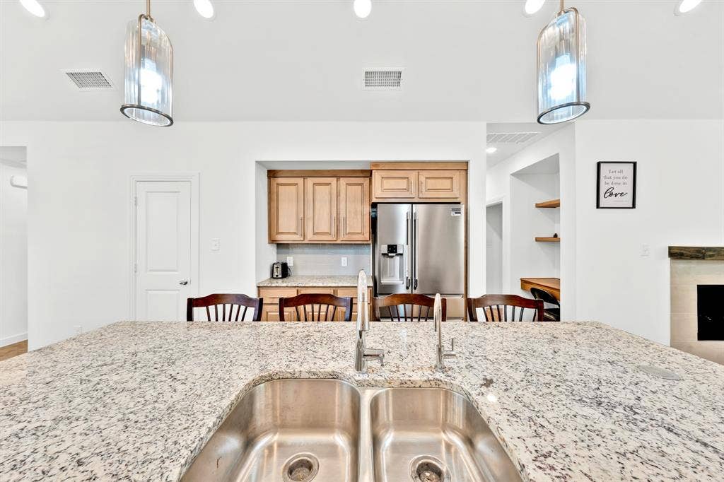 3928 Bison Lane, Crandall, TX 75114 Kitchen island with a double stainless steel sink and granite countertop, stainless steel refrigerator, and wood cabinetry