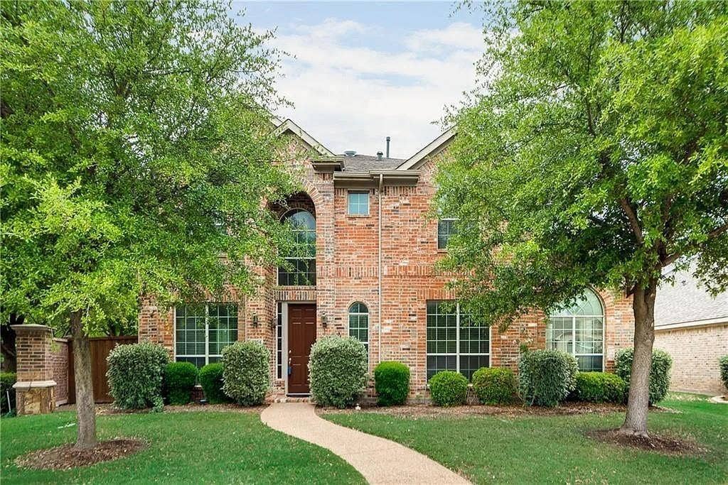 9304 Regal Oaks Drive, McKinney, TX 75072 Brick exterior with an arched entry window, a covered entryway, mature trees, manicured landscaping, and a winding pathway
