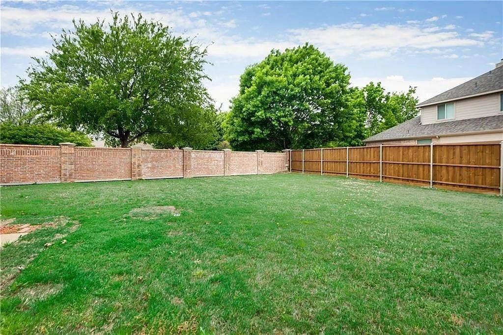 9304 Regal Oaks Drive, McKinney, TX 75072 Expansive grassy yard with a brick perimeter wall, wood privacy fence, and mature trees