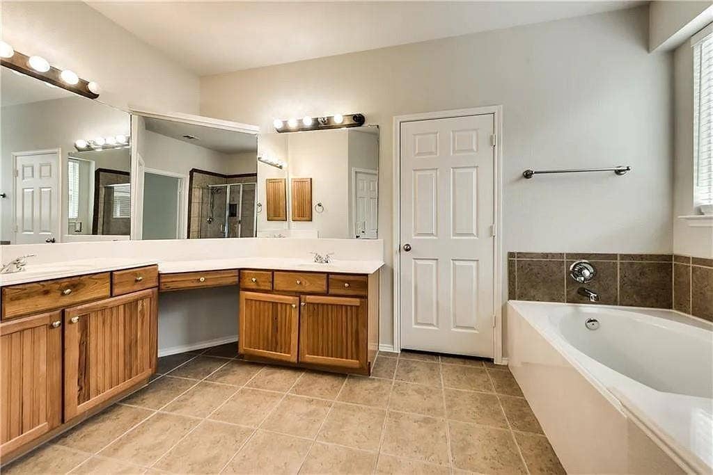9304 Regal Oaks Drive, McKinney, TX 75072 Dual vanities with integrated sinks, wood-finish cabinetry, ceramic tile flooring, built-in bathtub, and horizontal blinds