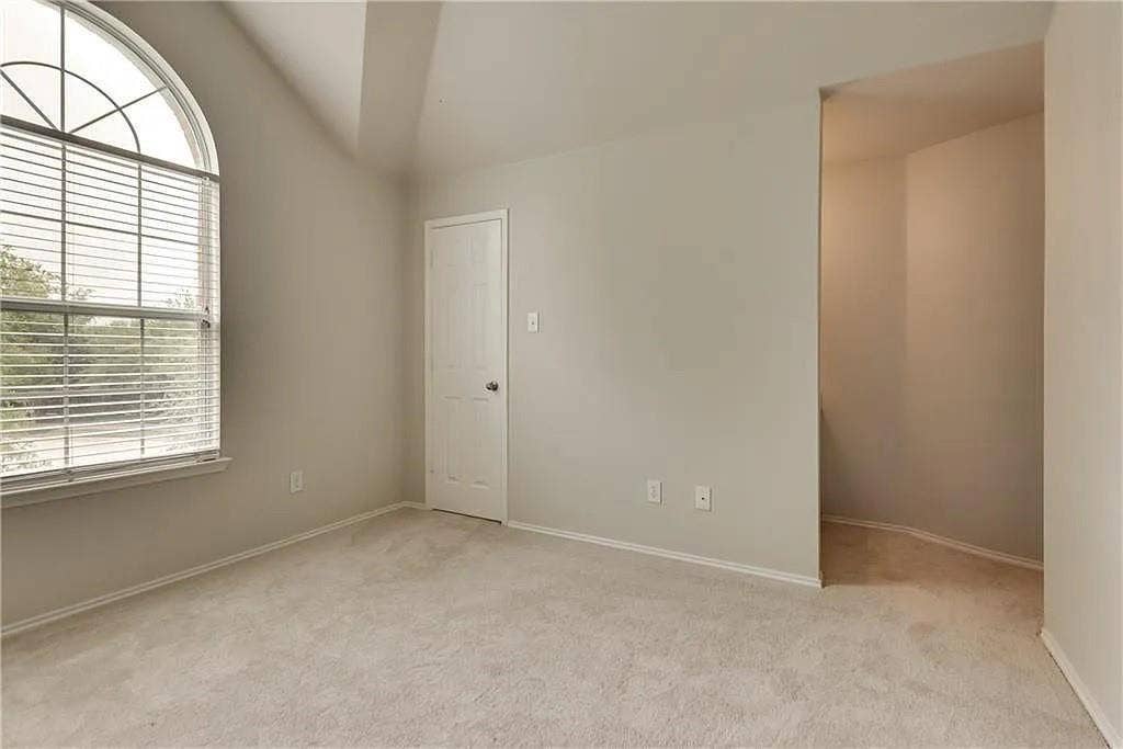 9304 Regal Oaks Drive, McKinney, TX 75072 Arched window with blinds, vaulted ceiling, neutral wall paint, light-colored carpeting, and a white paneled door