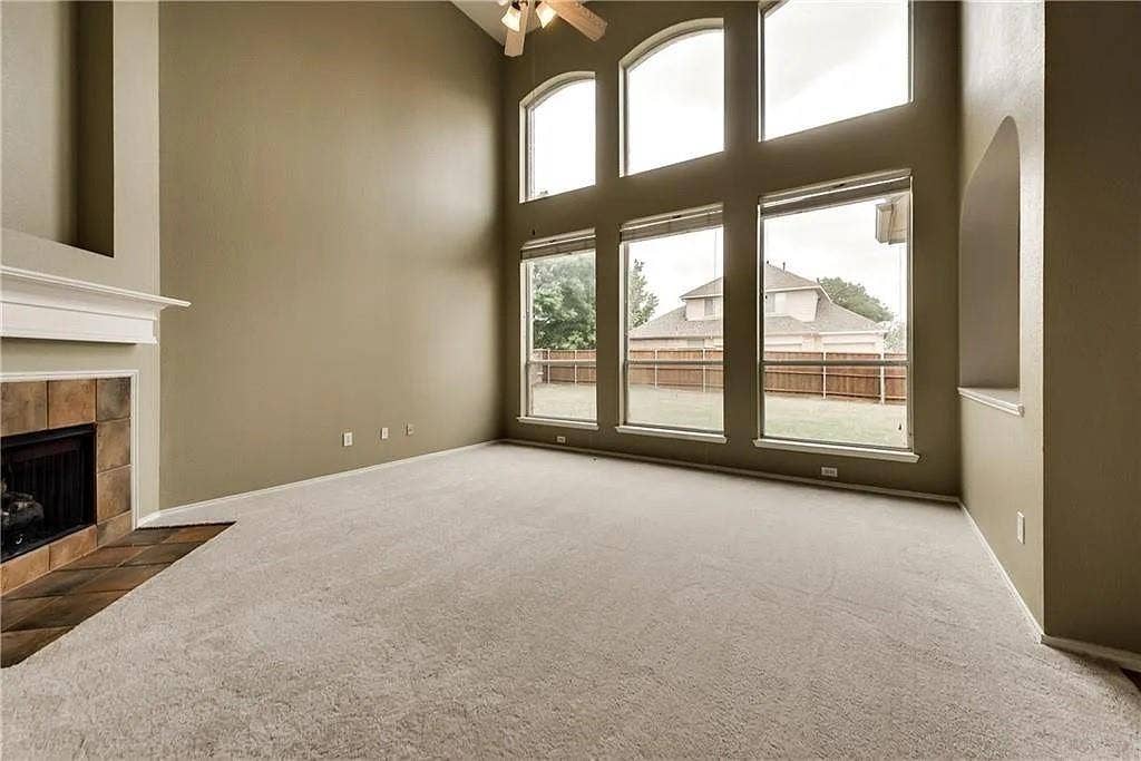 9304 Regal Oaks Drive, McKinney, TX 75072 Vaulted ceiling with ceiling fan, large arched windows, tile-surround fireplace with mantel, and carpeted flooring