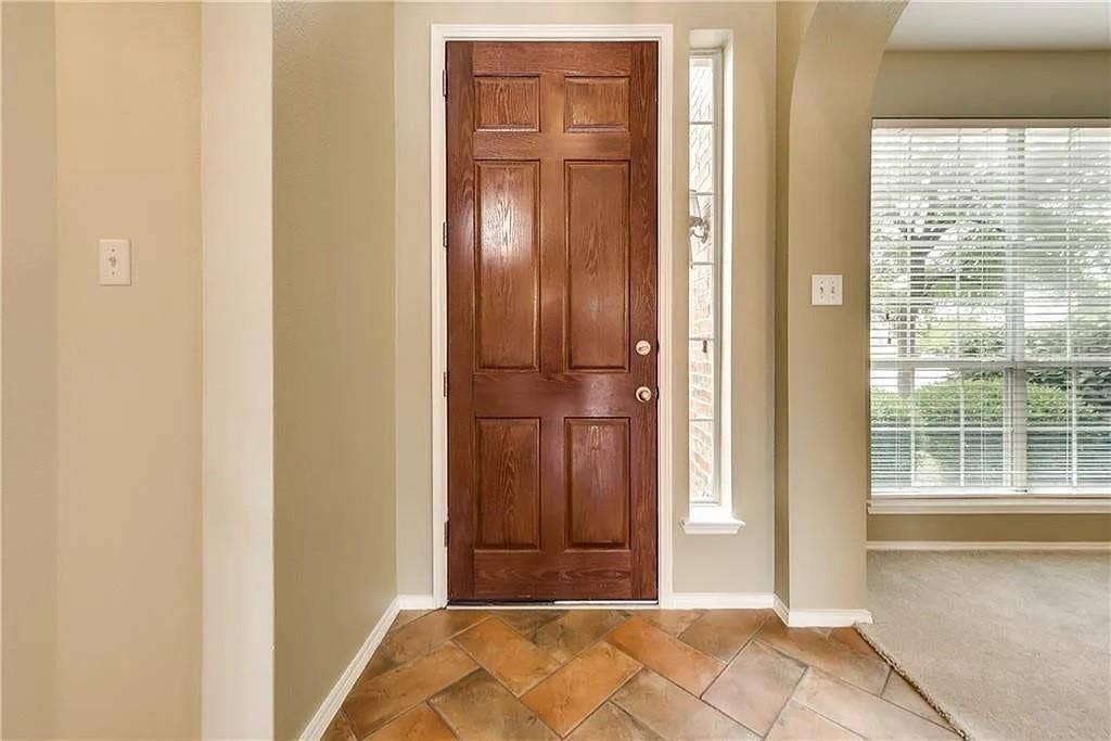 9304 Regal Oaks Drive, McKinney, TX 75072 Wood-paneled entry door with sidelight, terra cotta-toned tile flooring, and arched doorway