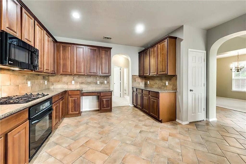 9304 Regal Oaks Drive, McKinney, TX 75072 Tile flooring in a herringbone pattern, extensive wood cabinetry, built-in microwave, gas cooktop, and arched doorways