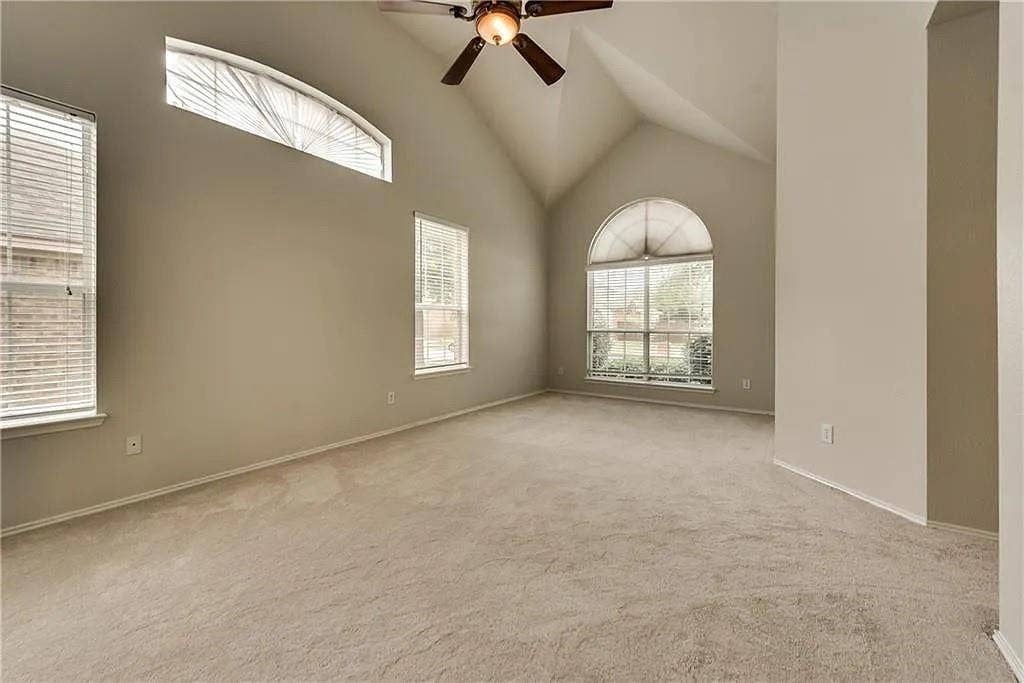 9304 Regal Oaks Drive, McKinney, TX 75072 Vaulted ceiling with a ceiling fan, arched windows, rectangular windows with blinds, and neutral carpet flooring